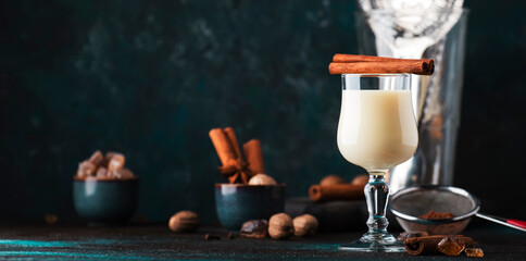 White Eggnog cocktail drink with milk, eggs and dark rum, sprinkled with cinnamon and nutmeg in shot glass on dark background, copy space