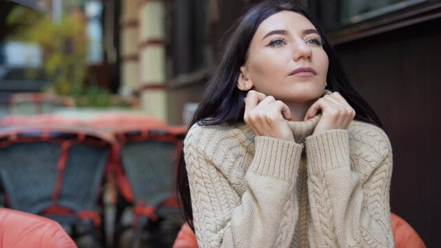 Caucasian girl model sitting in a street cafe, autumn rest on the terrace, woman enjoying vacation time, confiding smile to the camera.