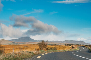 Small S shape asphalt road in a country side. Croagh Patrick mountain on the left in clouds. Travel in Ireland. county Mayo. Stunning Irish landscape. Cloud over peak looks like volcano eruption.