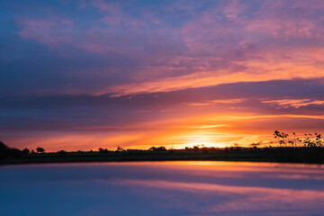 Obraz premium Stunning sunrise in a country side. Rich blue and orange colors of the sky. Silhouette of trees on horizon. Nature landscape scene. Calm atmospheric mood