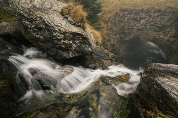 Small river flowing through some rocks and under a bridge near Transfagarasan Road in Romania