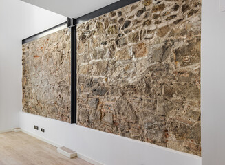 Restored ancient wall left from old city buildings in Barcelona. Interior of empty renovated apartment with stone wall.