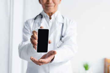 Cropped view of smartphone in hands of blurred doctor in clinic