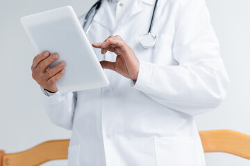 Cropped view of doctor in white coat using digital tablet in clinic