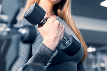 girl lifts a dumbbell, the process of training a girl in a gray suit for fitness. the background is...