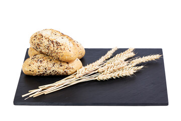 Baguettes with seeds next to some ears of wheat on a black slate board. Food concept