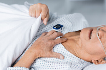Cropped view of sick senior man with nasal cannula and pulse oximeter lying on bed in clinic