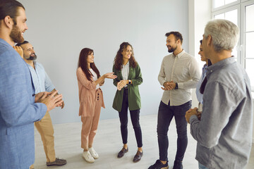 Happy young and mature people having friendly conversation at business event. Group of men and women meeting with business coach. Team of employees standing in office and having interesting discussion - Powered by Adobe