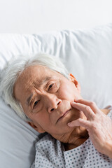 Elderly asian patient looking at camera while lying on bed in clinic