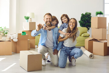 Fototapeta na wymiar Happy family showing keys to new home on moving day. Portrait of mum, little kids and dad looking at camera and laughing in living room with unpacked cardboard boxes. Buying house or apartment concept