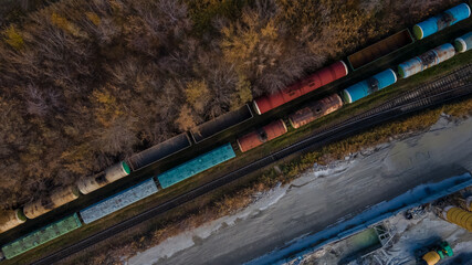 Fototapeta premium Aerial view of railroad in beautiful forest at sunset in autumn. Industrial landscape with railway station, trees with orange leaves in fall. Top view of rural railway platform. Transportation