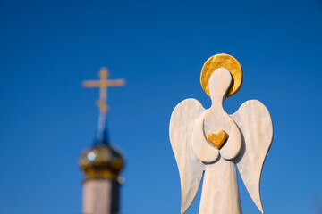 Wooden figure of an angel with a golden heart in his hands on a church and blue sky background. 