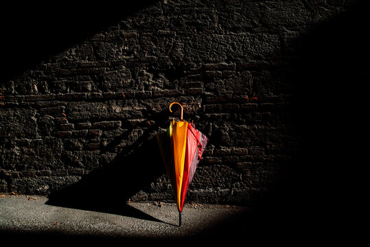 A beautiful colored umbrella rests folded against a brick wall illuminated by the first rays of sun after the rain.