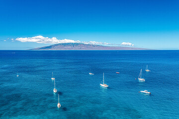 Aerial shot of sailboats in Lahaina, Maui, Hawaii with teal water on calm blue sky day