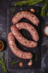 Raw sausages and ingredients for cooking on a black stone table.