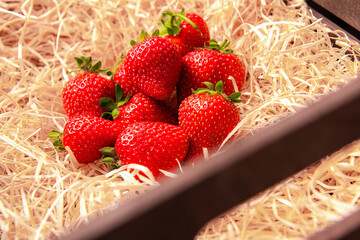 ripe strawberries are lying in a box on wood shavings