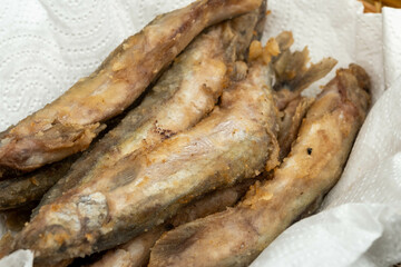 Fried fish on a paper napkin in a wicker basket on a wooden table.