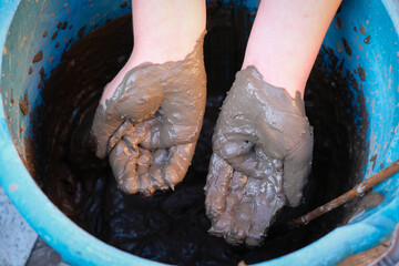 Black mud on a child's hands. The child plays with clay in a blue bucket. Funny photo.