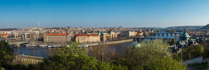 Wide panoramic aerial view of Prague Old Town architecture roof top and Charles Bridge over Vltava river seen from Letna hill park, spring sunny day, blue sky, Czech Republic