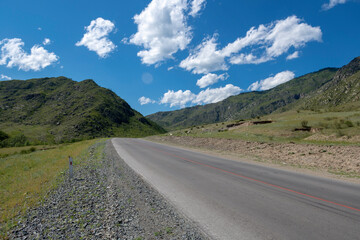 Fototapeta na wymiar peaks of mountains against the sky with white clouds. Summer sunny day. Mountain asphalt road