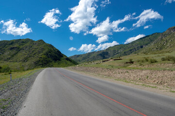 peaks of mountains against the sky with white clouds. Summer sunny day. Mountain asphalt road