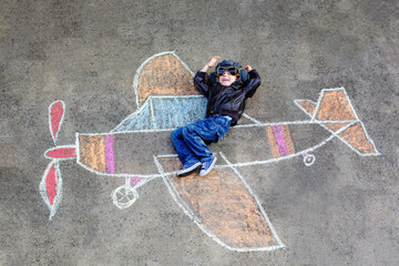 Little preschool boy painting plane with colorful chalks and dreaming be a pilot. Creative leisure...