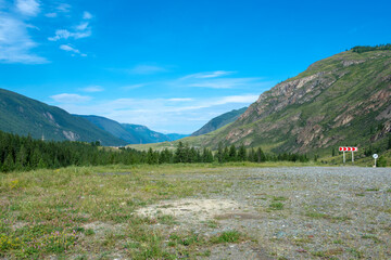 peaks of mountains against the sky with white clouds. Summer sunny day. Mountain asphalt road