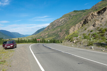 passenger red car parked on a mountain road among high rocks. Summer clear day