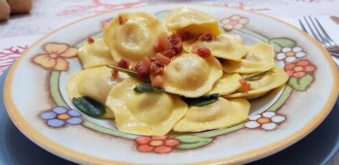 Ravioli ripieni di carne cotti con burro e salvia e guarniti con pancetta a cubetti