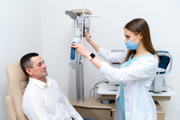Female optometrist doing sight testing for male patient in hospital. Modern equipment in...