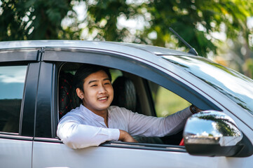 A man driving a car opens the window and smiles.