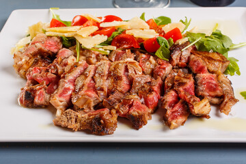 Tagliata di carne cotta al sangue e guarnita con rucola, scaglie di parmigiano e pomodori