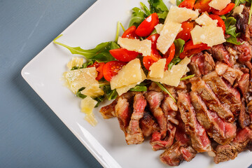 Tagliata di carne cotta al sangue e guarnita con rucola, scaglie di parmigiano e pomodori fotografata dall'alto