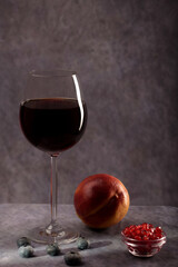 A simple still life. A beautiful glass of red wine, a plate with pomegranate seeds and a peach on a dark background with creative lighting