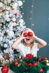 Santa little helper with decorative christmas tree on background. Little girl have fun play with red balls. Christmas and new year concept