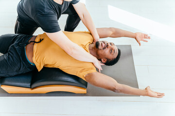 Fototapeta na wymiar Young fit african american man is concentrated on exercise on pilates reformer bed with male instructor at gym. Sports equipment. Active and healthy lifestyle rehabilitation concept.