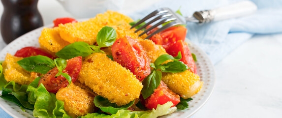 Fried cheese slices in corn grits, cooked tomatoes and lettuce on a light background. breakfast concept. Selective focus