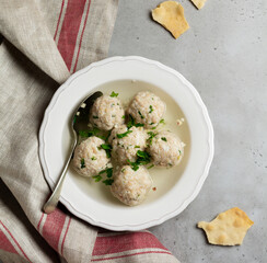 Homemade chicken matzo ball soup with parsley and garlic in simple white ceramic plate on a gray stone or concrete background. Traditional Jewish passover dish. Selective focus. Top view