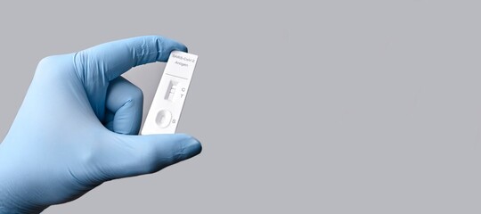 Gloved hand holding a positive rapid test device for COVID-19. Panoramic image with copy space.	