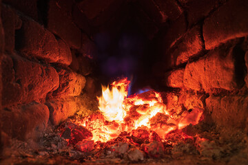 Hot coals inside an old rustic brick oven. There are yellow and blue flames. Background. Texture.