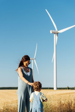 Beautiful middle aged young mother woman in wind farm with windmills in background with her three year old son. renewable energy concept