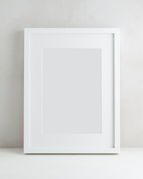 Empty white frame with passe-partout on the background of a light wall. Mock up poster with a place for your design in a minimalistic interior.