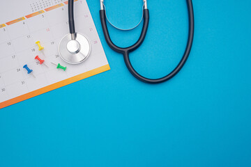 A stethoscope and calendar page date isolated on blue background. Doctor appointment schedule. Top View. Space for text