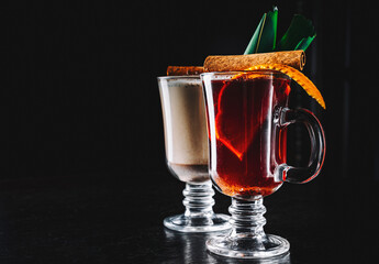 mulled wine with spices and orange slices on rustic wooden table on dark background