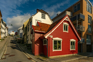 kleines, altes rotes Haus mit weissen Fensterrahmen in Bergen, Norwegen, das zwischen grossen neueren Häusern in der Altstadt steht. herziges, echt nordisches Häuschen mit Stil. norwegischer Flair 