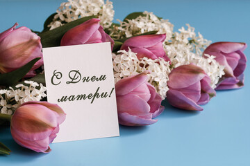 Postcard with the text in Russian Happy Mother's Day and a bouquet of beautiful flowers on a blue...