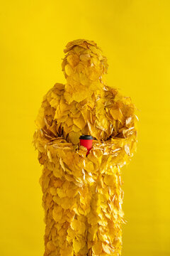 Woman with leaf costume and disposable cup in front of yellow background