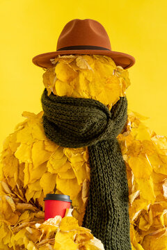 Woman wearing leaf costume holding disposable cup by yellow background