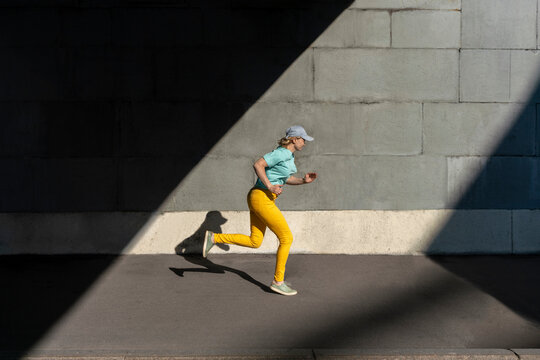 Mid adult woman wearing cap running on road during sunny day