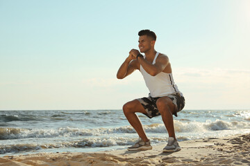 Sporty man doing exercise on sandy beach at sunset